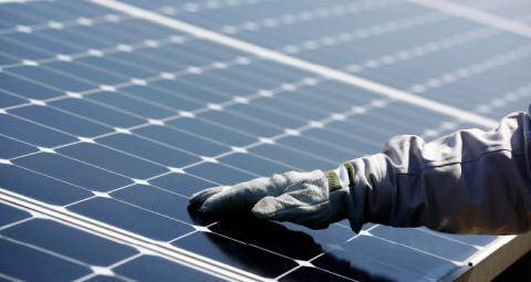 يد ترتدي قفازاً على لوحة شمسية لمحطة الطاقة الفولتضوئية تم إنشاؤها بواسطة مجموعة هندسة البرمجيات الذكية (ISE)، توتال وصن باور في ناناو، اليابان.

